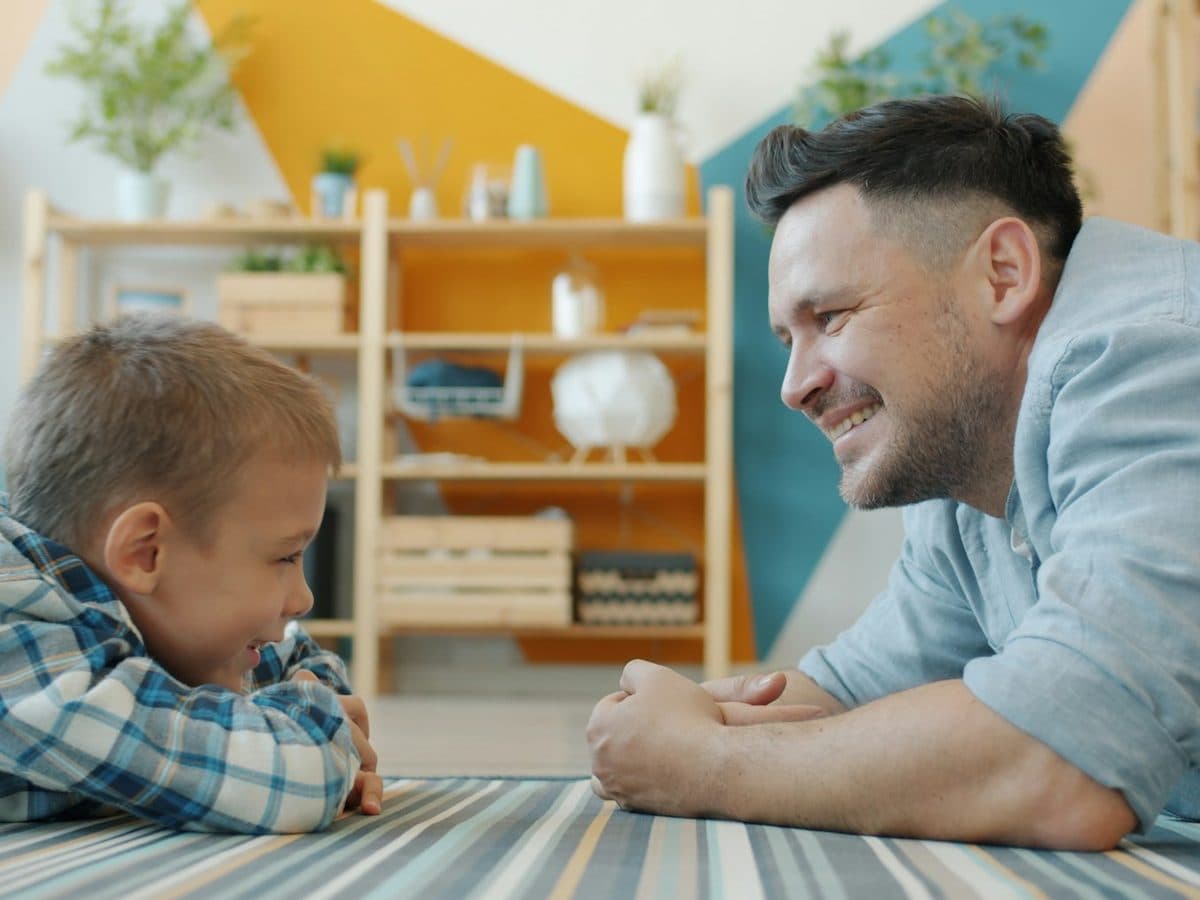 An adult and a child sitting face to face on the floor of a bright room