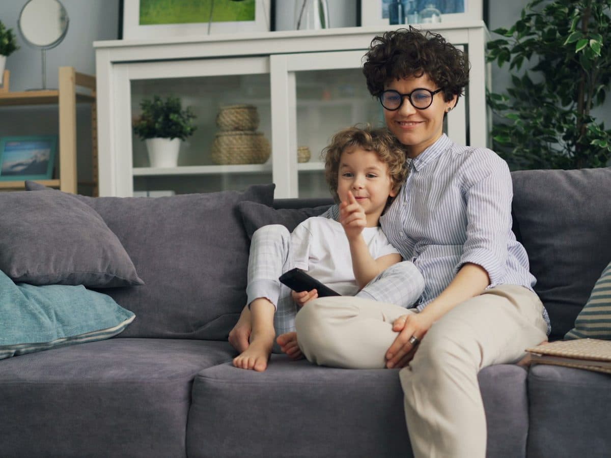 A carer and a small child sitting together on the sofa at home
