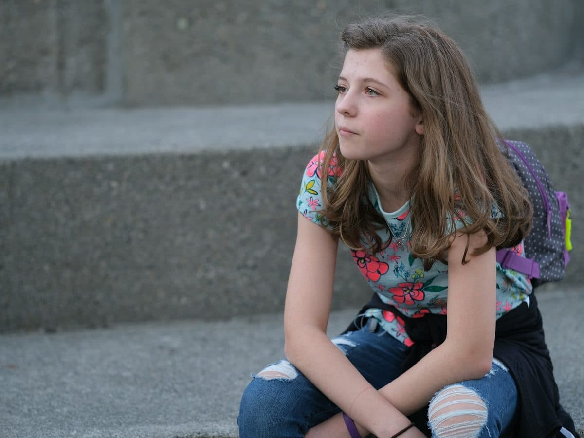 A young person sitting on steps with a backpack beside them