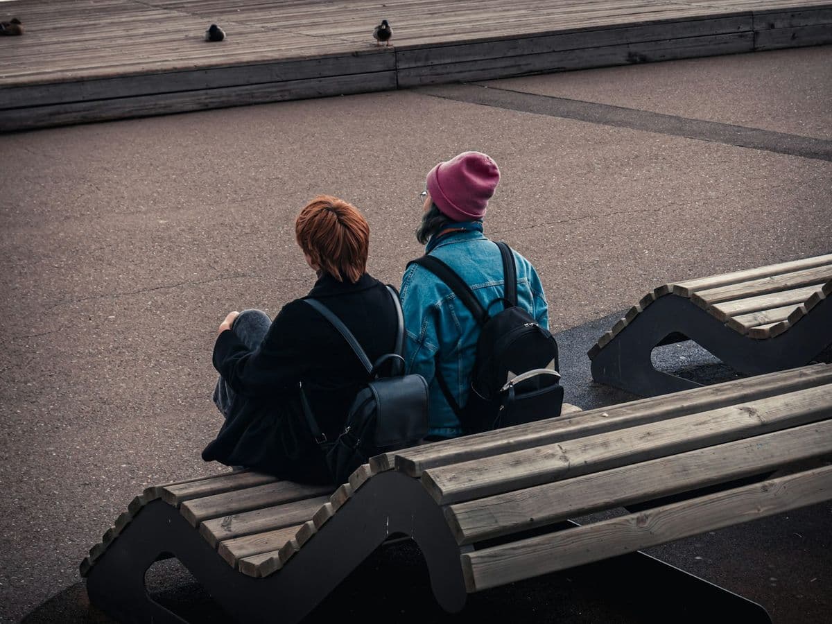 Two young people sitting side by side on a bench, seen from behind
