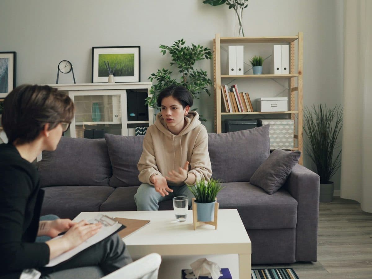 A practitioner with a clipboard listening to a young person on a sofa